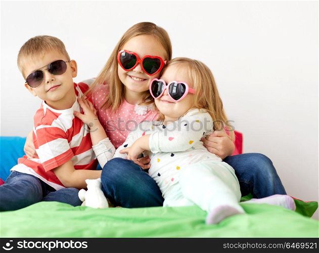 summer, valentines day and childhood concept - happy little kids in heart shaped sunglasses at home. happy little kids in sunglasses at home