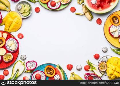 Summer various colorful sliced tropical fruits and berries in plates and bowls on white  background, top view, frame. Clean and healthy lifestyle  background