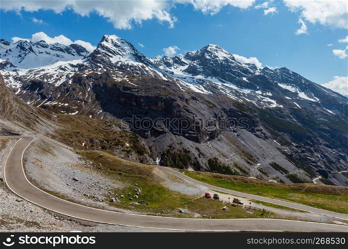 Summer view from Stelvio Pass alpine road with fir forest and snow on Alps mountain tops, Italy. Cars model are unrecognizable.