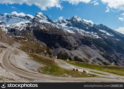 Summer view from Stelvio Pass alpine road with fir forest and snow on Alps mountain tops, Italy. Cars model are unrecognizable.