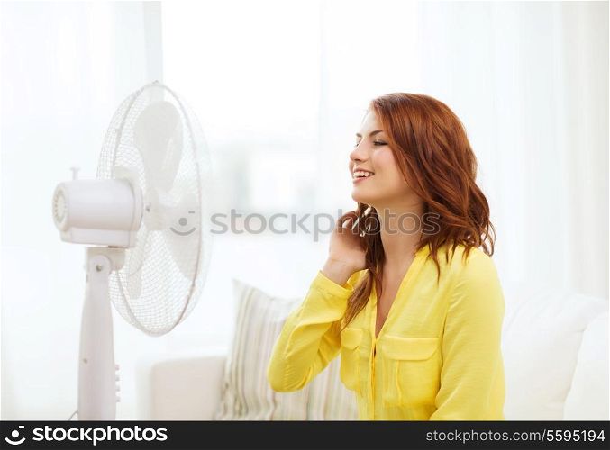 summer, weather and equipemt concept - smiling redhead teenage girl with big fan at home