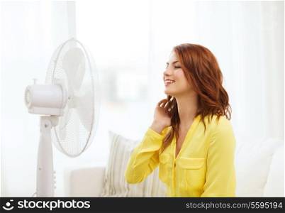 summer, weather and equipemt concept - smiling redhead teenage girl with big fan at home
