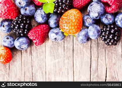 Summer wild berries over shabby wooden background. Raspberry, strawberry, blackberry and blueberry on the table