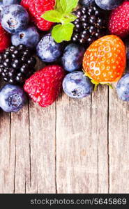 Summer wild berries over shabby wooden background. Raspberry, strawberry, blackberry and blueberry on the table