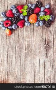 Summer wild berries over shabby wooden background. Raspberry, strawberry, blackberry and blueberry on the table