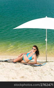 Summer woman in bikini alone on beach sunbathing under parasol