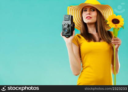 summer woman wearing yellow dress and hat with sunflower and old vintage camera in hand on vivid blue background
