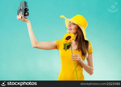 summer woman wearing yellow dress and hat with sunflower taking self picture with old vintage camera on vivid blue background