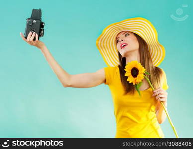 summer woman wearing yellow dress and hat with sunflower taking self picture with old vintage camera on vivid blue background