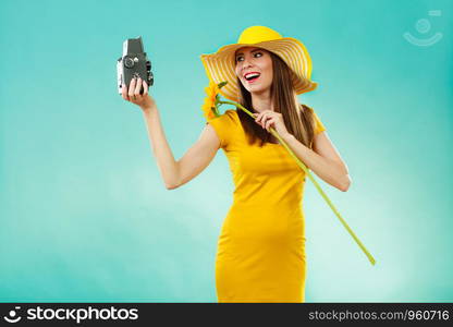 summer woman wearing yellow dress and hat with sunflower taking self picture with old vintage camera on vivid blue background