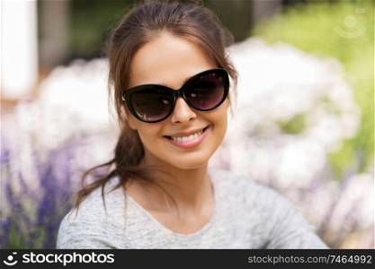 summertime, leisure and people concept - portrait of happy young woman in sunglasses at summer garden. happy young woman in sunglasses at summer garden