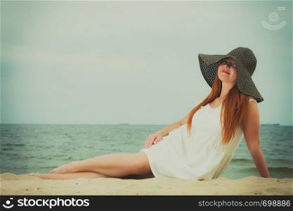 Summertime outfit accessories concept. Happy redhead woman wearing big black sun hat lying on beach during summer.. Redhead woman wearing sun hat lying on beach