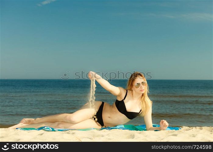 Summertime pleasures, enjoying vacation concept. Woman in bikini sunbathing and relaxing on beach, playing with sand.. Woman in bikini sunbathing and relaxing on beach