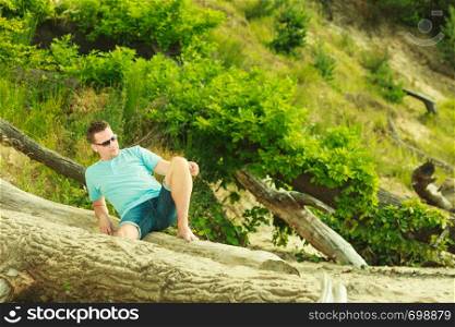 Summertime relaxation, vacation and holiday, adventure traveling concept. Handsome man sitting on tree trunk relaxing during summer.. Handsome man relaxing on beach during summer.