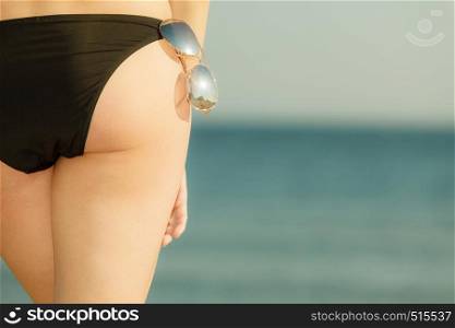 Summertime underwear, being confident during summer concept. Woman bottom bum in black bikini panties and glasses. Sea background.. Woman bottom in black bikini panties and glasses