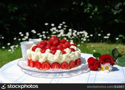 Summertime with strawberry cake and two mugs on a table in a garden