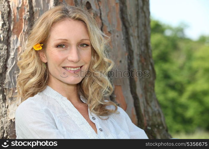 Summery woman with a flower in her hair sitting against a tree trunk