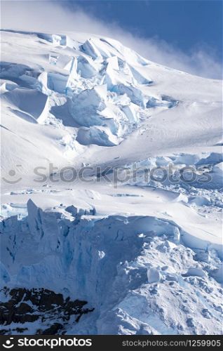 Summit of mountain with blue snow and layer of ice overlaid very close against sky in Antarctica