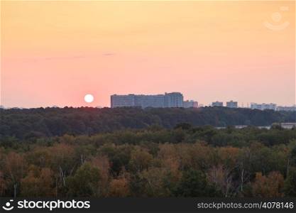 sun above horizon during red sunrise over houses and urban park in summer morning