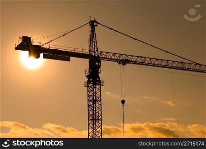 Sun behind a crane at a construction site at evening