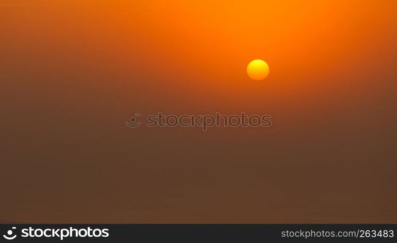 Sun behind fog or clouds during sunset by beach. Orange moody colors. Bright sun during sunset