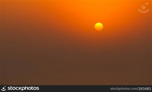 Sun behind fog or clouds during sunset by beach. Orange moody colors. Bright sun during sunset
