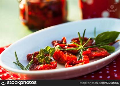 sun dried tomatoes on a white plate with fresh herbs - rosemary, basil and oregano