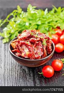 Sun-dried tomatoes with thyme and basil in a bowl, fresh small tomatoes, parsley on wooden board background