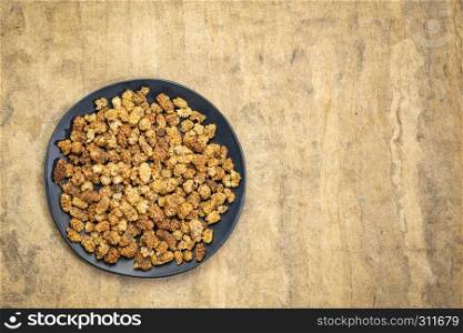 sun-dried white mulberry berries on a black plate against textured bark paper with a copy space