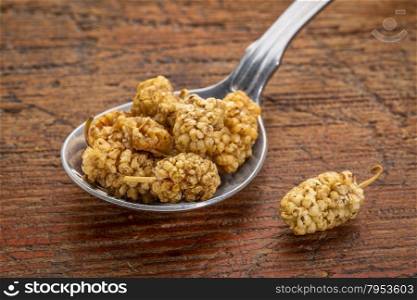 sun-dried white mulberry berries on a tablespoon against rustic wood
