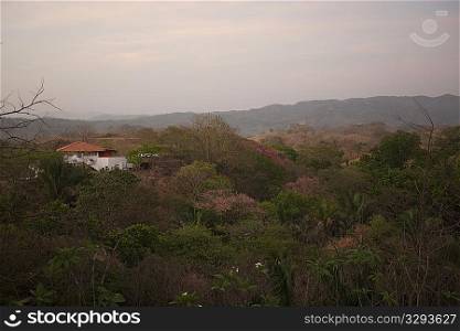 Sun fading over a white house with an orange roof in the rolling hills above the treetops of Costa Rica