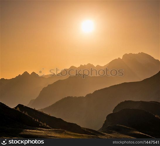 Sun glow in evening hazy sky and mountain silhouettes view. Peaceful view from Giau Pass. Climate, environment and travel concept scene.