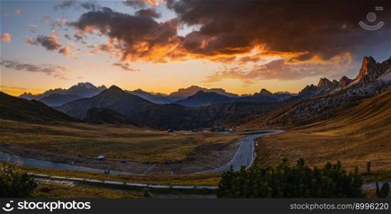 Sun glow in evening hazy sky. Italian Dolomites mountain silhouettes panoramic peaceful view from Giau Pass. Climate, environment and travel concept scene. Cars unrecognizable.