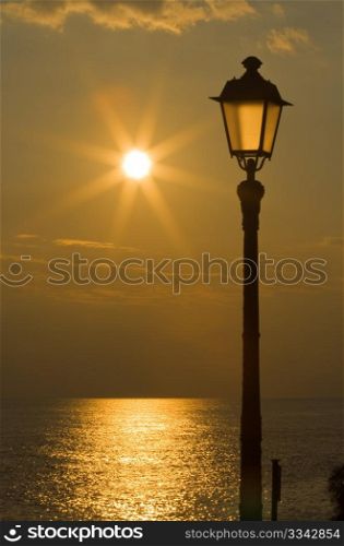 Sun is reflected on the sea and streetlight at sunset