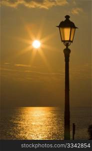 Sun is reflected on the sea and streetlight at sunset