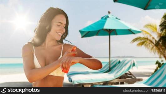 sun protection, tanning and beauty concept - happy smiling young woman in bikini swimsuit using sunscreen spray over tropical beach background in french polynesia. smiling woman in bikini with sunscreen on beach