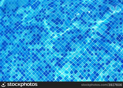 Sun reflection on the blue clear water ripples of swimming pool with mosaic bottom