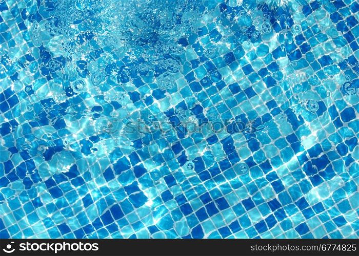 Sun reflection on the blue clear water ripples of swimming pool with mosaic bottom