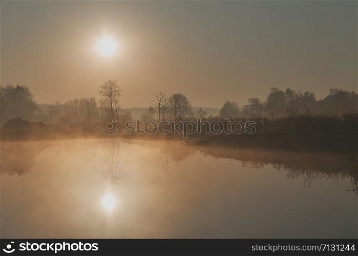 Sun rising above field and pond flooded with fog in the morning