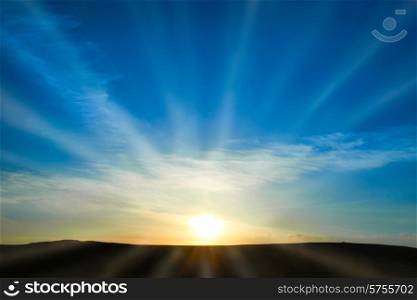 Sun rising above the land on blue sky. Nature background with sunny beams