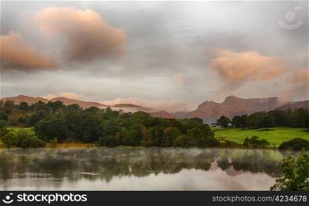 Sun rising and illuminating Langdale Pikes with Loughrigg Tarn in foreground