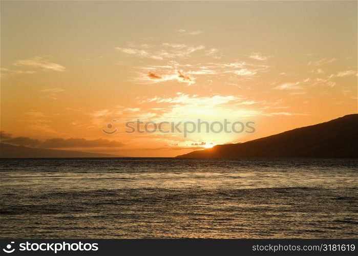 Sun setting behind island off Maui, Hawaii.