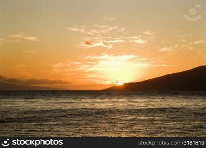 Sun setting behind island off Maui, Hawaii.