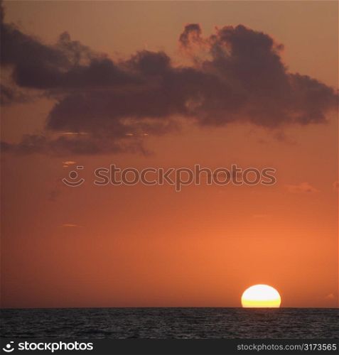 Sun setting over horizon of ocean.