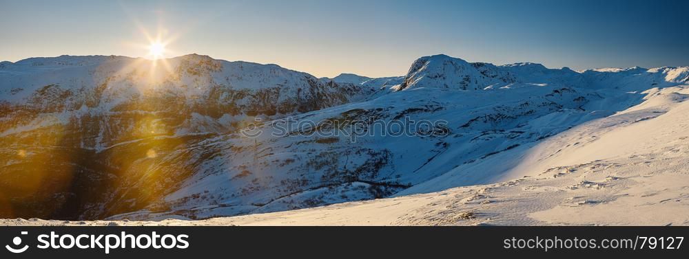 Sun setting over mountain range covered with snow. Norway.
