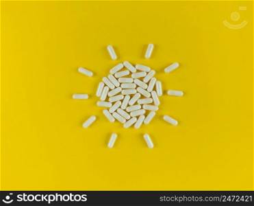 Sun shape made from white pills capsules on a yellow backdrop.. Sun shape made from white pills capsules on yellow backdrop.