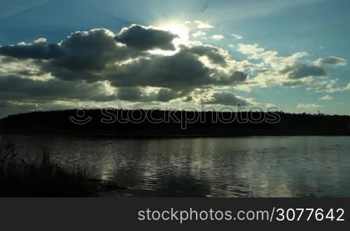 sun shines through the clouds above the lake