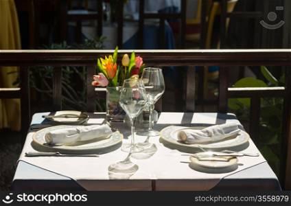 Sun shining on white tablecloth place setting in restaurant by beach