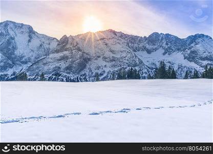 Sun shining over mountain peaks and snow - Lovely winter scenery with the Austrian Alps mountains covered in snow, the trees line and a route from footsteps in the snow.