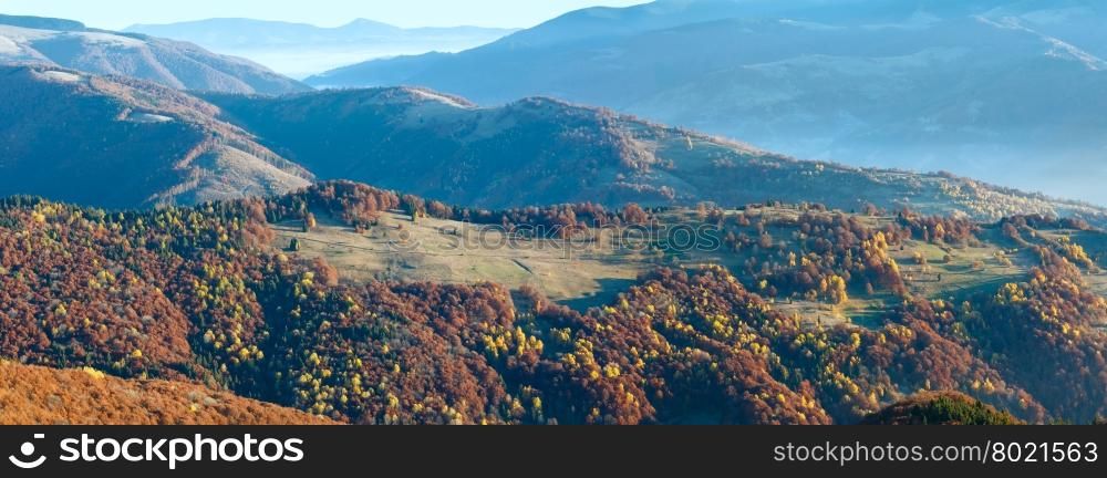 Sunbeam and autumn misty morning mountain panorama with colorful trees on slope.